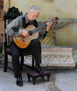 carlos gonzales sitting in chair playing guitar in front of fountain