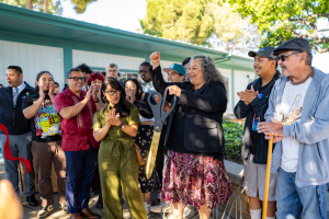 A group of staff, faculty, and administrators holding large ceremonial scissors as they cut the red ribbon in front of the Art + Design Complex