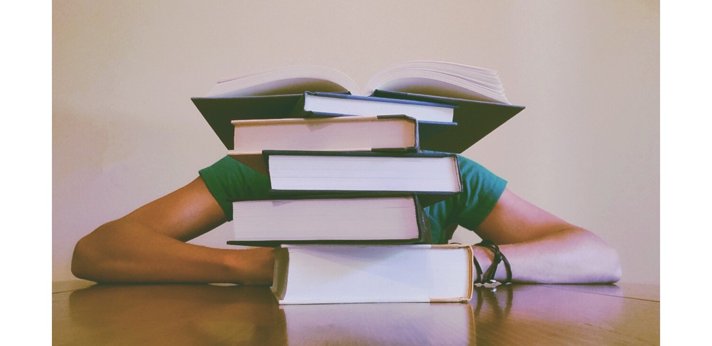 student hiding behind stack of books