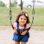 Little girl leaning on a swing at an outdoor park. 