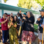 A group of staff, faculty, and administrators holding large ceremonial scissors as they cut the red ribbon in front of the Art + Design Complex