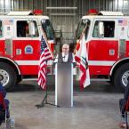 Oxnard College Fire Academy Founder Ed French speaks at dedication event standing at a podium in front of two fire engines, the American flag, and the California flag.