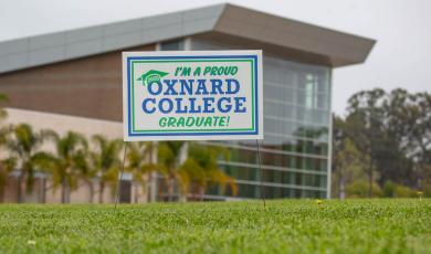 A yard sign that says "I'm a proud Oxnard College Graduate!" on the lawn in front of the Oxnard College Performing Arts Building.