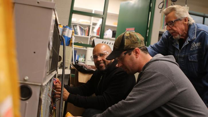 two students receiving critique from the HVAC professor while fixing an air conditioning unit