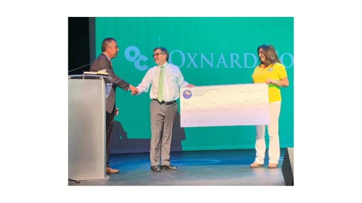 Robert Cabral shaking President Sanchez's hand, who is holding a large check poster with Connie Owens to recognize the OCF textbook donation