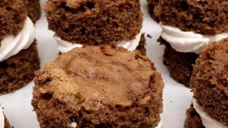 round chocolate cake cookie sandwiches with whipped cream filling. Rows of cookie sandwiches displayed on stainless steel baking sheet.