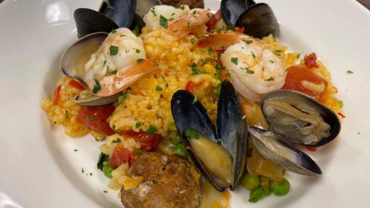 clams, scallops, and shrimp on bed of cajun rice gumbo plated on white plate