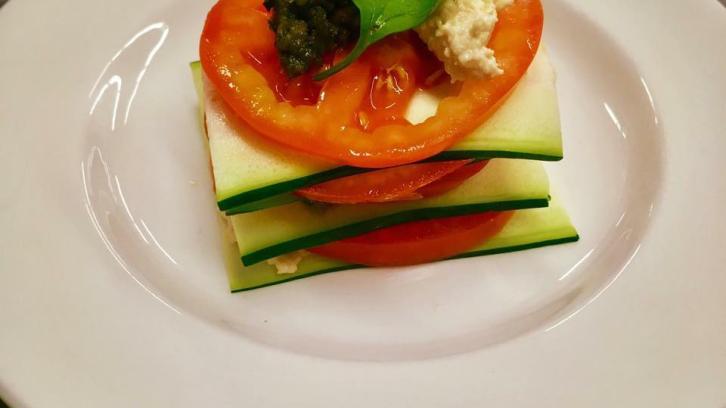 tomato salad stacked with zucchini wafers, topped with garnish plated on white plate