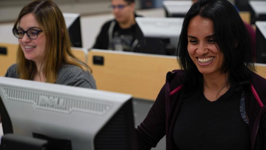 two smiling female students sitting in front of computers