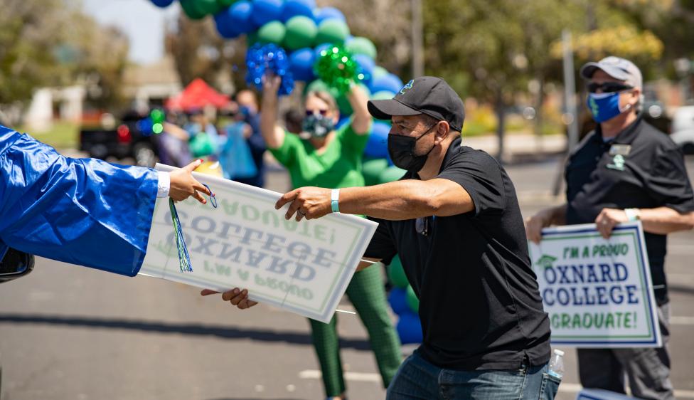 Oxnard College staff handing a Class of 2021 sign to a graduate