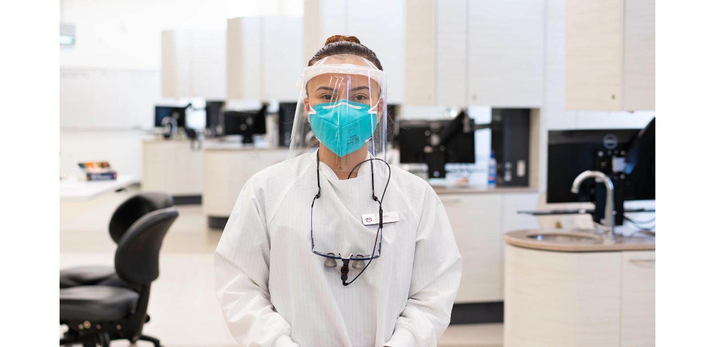 female student standing in foreground of Dental Hygiene laboratory facility wearing PPE for Dental Hygiene