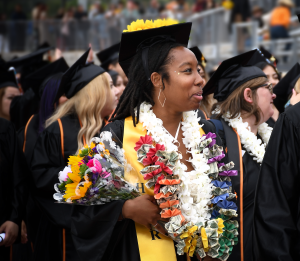 A smiling graduate holds a bouquet and wears colorful leis a A smiling graduate holds a bouquet and wears colorful leis a