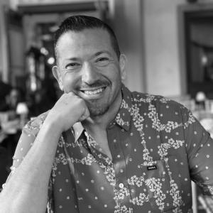 Damien Peña, a man with short dark hair wearing a floral shi Damien Peña, a man with short dark hair wearing a floral shi