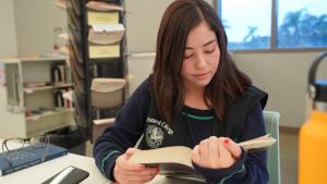 Young student wearing Oxnard College vest reading textbook i Young student wearing Oxnard College vest reading textbook i