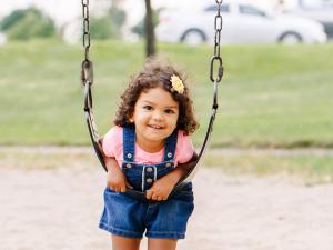 Little girl leaning on a swing at an outdoor park.